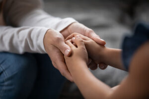 Close up compassionate young foster parent holding hands of little kid girl. Private investigator New Orleans