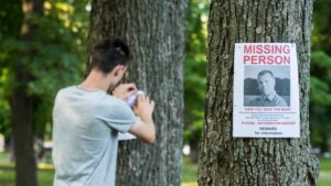 A young man puts up ads for a missing person in the park. Showing the need of a private investigator New Orleans.